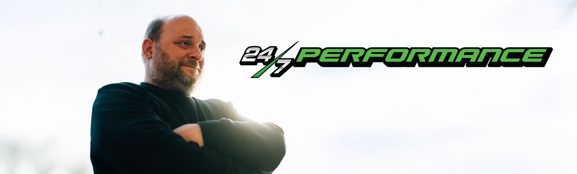 Der Firmeninhaber Karl Brod von 24/7 Performance mit verschränkten Armen neben seinem Logo.