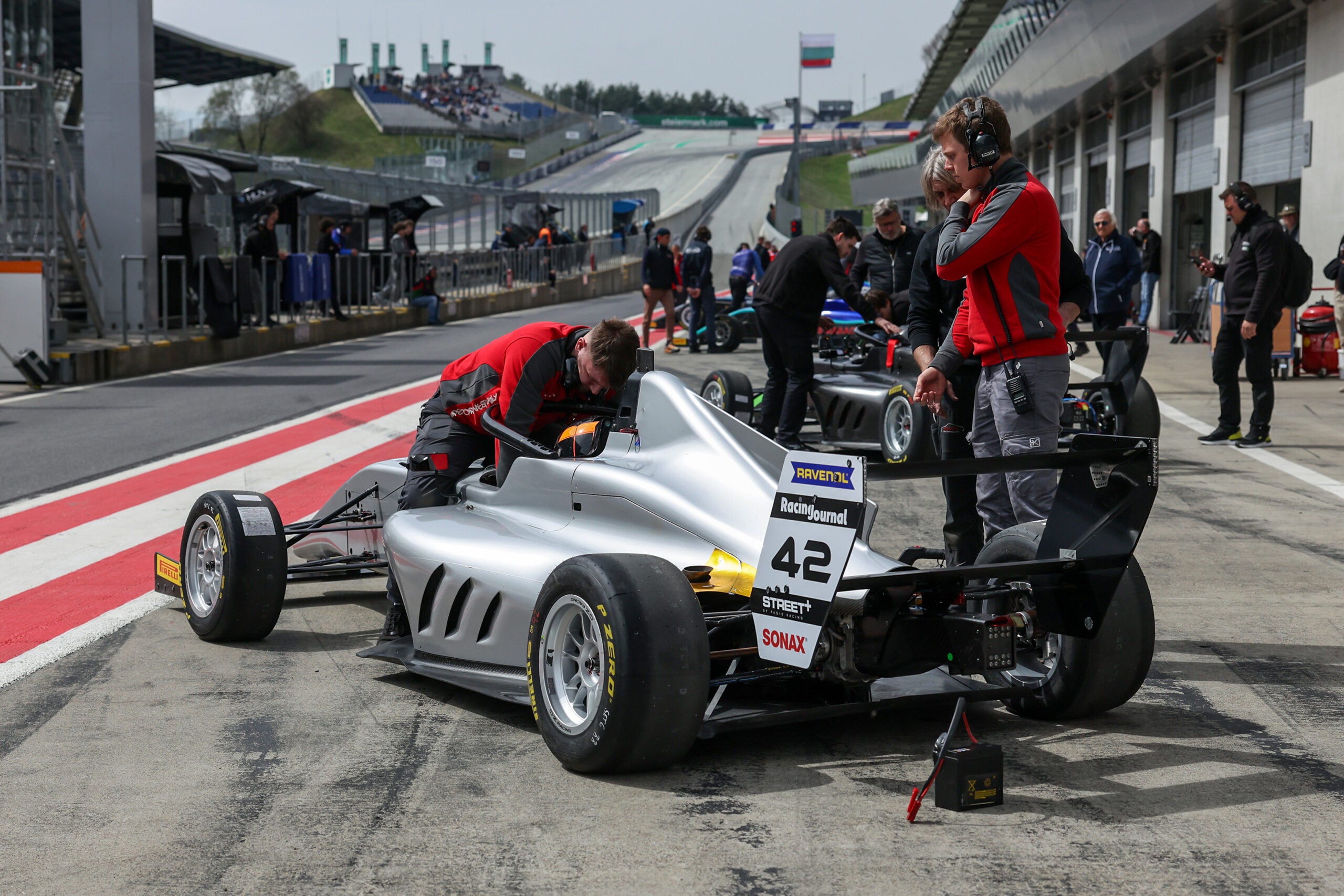 Mechaniker arbeiten in der Boxengasse an einem silbernen Formel 4 Fahrzeug mit der Startnummer 42 während eines Rennwochenendes.