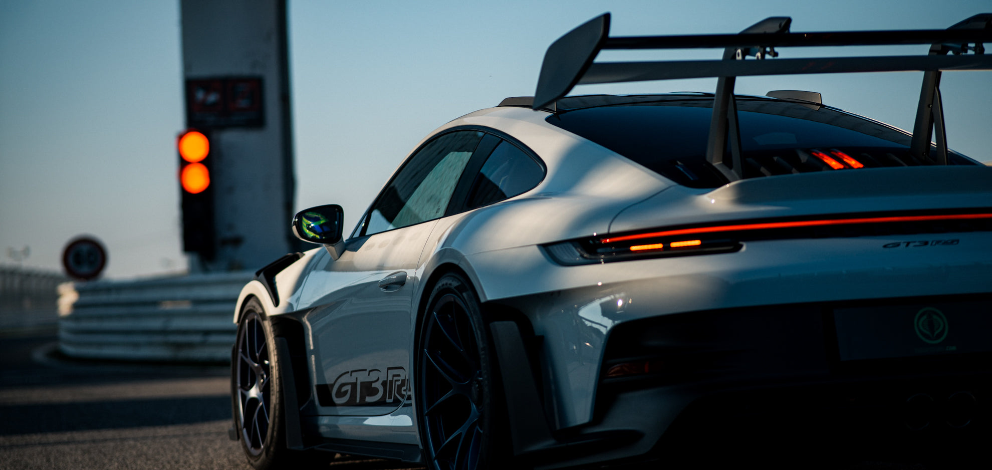 Weißer Porsche 992 GT3 RS mit schwarzen Felgen an einer roten Boxenampel in einer Boxengasse auf einer Rennstrecke.