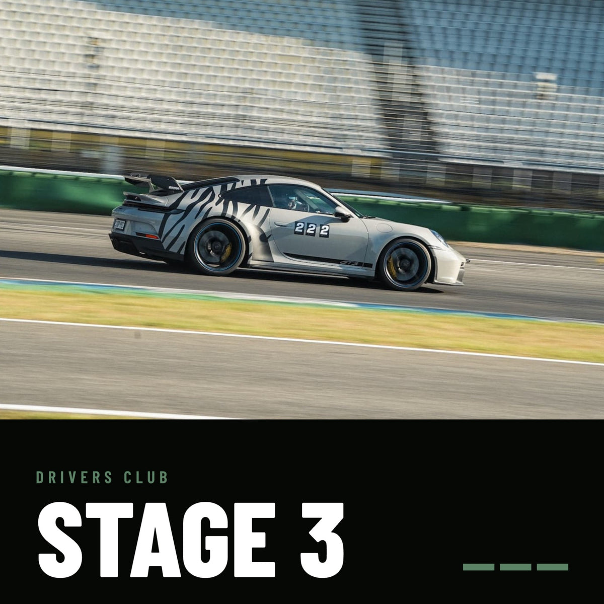 Drivers Club Stage 3: grauer Porsche 911 GT3 mit Zebra-Folierung und Startnummer 222 in voller Fahrt vor der Tribüne