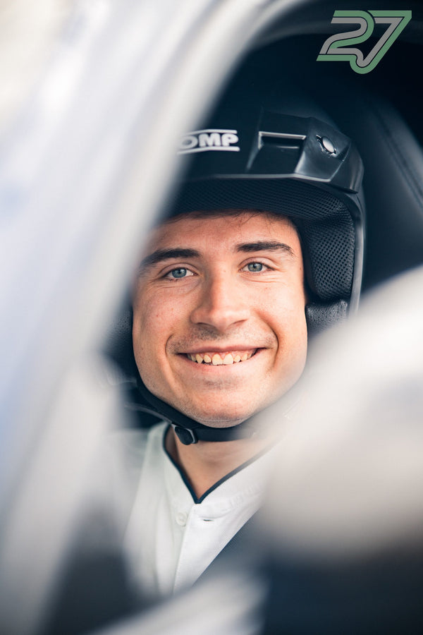 Ein junger Fahrer mit schwarzem Helm lächelt breit und blickt durch das Autofenster in die Kamera