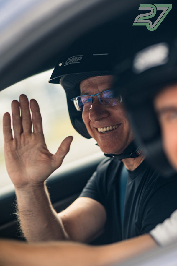 Ein Fahrer mit Helm und Brille lacht herzlich und streckt die Hand aus dem offenen Autofenster
