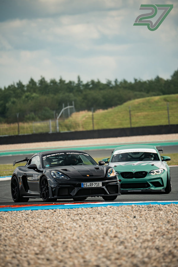 Dunkler Porsche Cayman GT4 zieht vor mintgrünem BMW M2 durch eine Kurve in Assen, beide dicht hintereinander