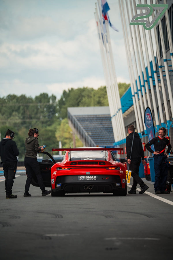 Boxencrew steht um einen roten Porsche-Rennwagen in der Boxengasse von Assen, Flaggen im Wind
