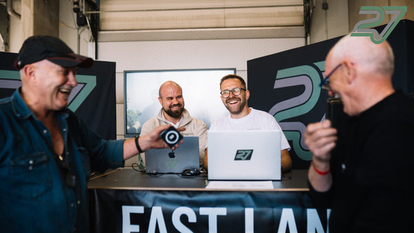 Vier Männer lachen ausgelassen an einem Tisch mit Laptops, im Hintergrund ein Banner mit Team-Schriftzug