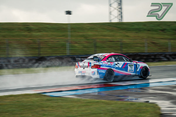 Weiß-pink-blauer BMW Rennwagen Nr. 79 zieht auf nasser Strecke eine Wasserfontäne hinter sich her