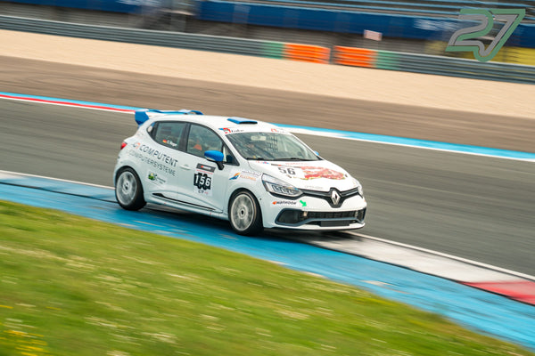 Weißer Renault Clio Cup rast am Randstreifen entlang, der verwischte Hintergrund zeigt das Tempo