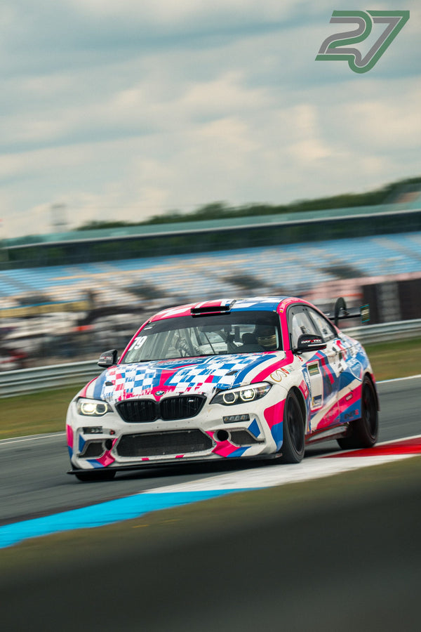 BMW M2 in auffälliger pink-blauer Karo-Lackierung kommt mit Blick zur Kamera aus der Kurve