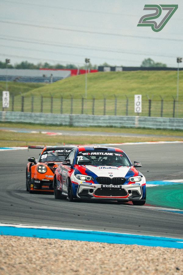 Weiß-blau-roter BMW M2 führt vor einem orangefarbenen Porsche 911 durch die Schikane