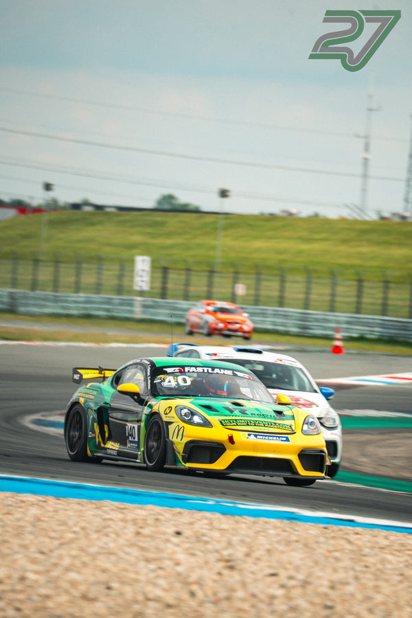 Gelb-grüner Porsche 718 Cayman GT4 fährt voraus, im Hintergrund verschwimmen ein weißer und ein oranger Rennwagen