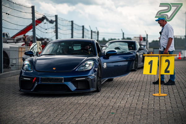 Dunkelblauer Porsche 718 Cayman GT4 rollt durch die Boxengasse an einem Streckenposten vorbei