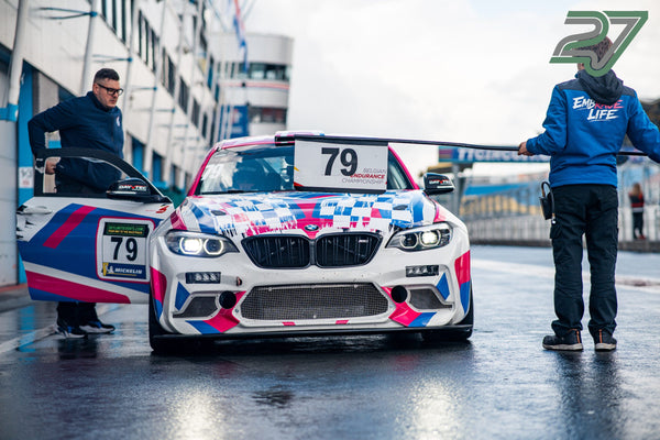Weiß-pink-blauer BMW Rennwagen Nr. 79 steht frontal in der Boxengasse auf nassem Asphalt