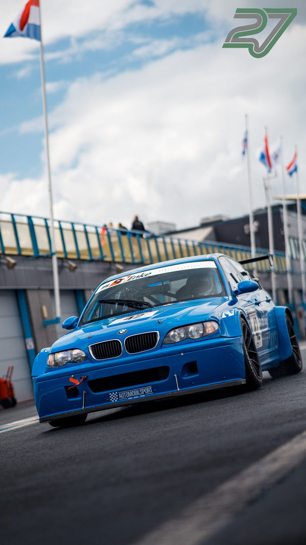 Blauer BMW E46 Rennwagen fährt frontal auf die Kamera zu, im Hintergrund Zuschauer auf der Brücke