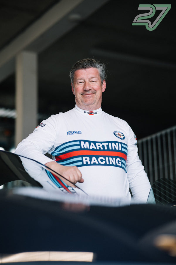 Ein Fahrer im weißen Martini-Racing-Trikot lächelt neben der geöffneten Fahrertür