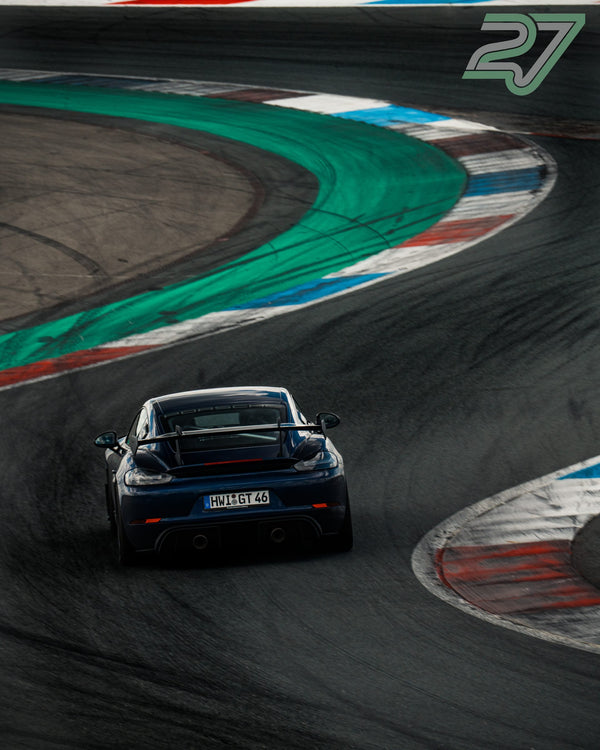 Dunkelblauer Porsche 718 Cayman GT4 fährt in Assen durch die bunten Curbs der Schikane