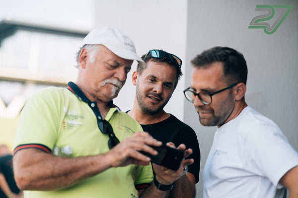 Drei Männer schauen konzentriert auf ein Smartphone-Display in der Boxengasse von Bilster Berg