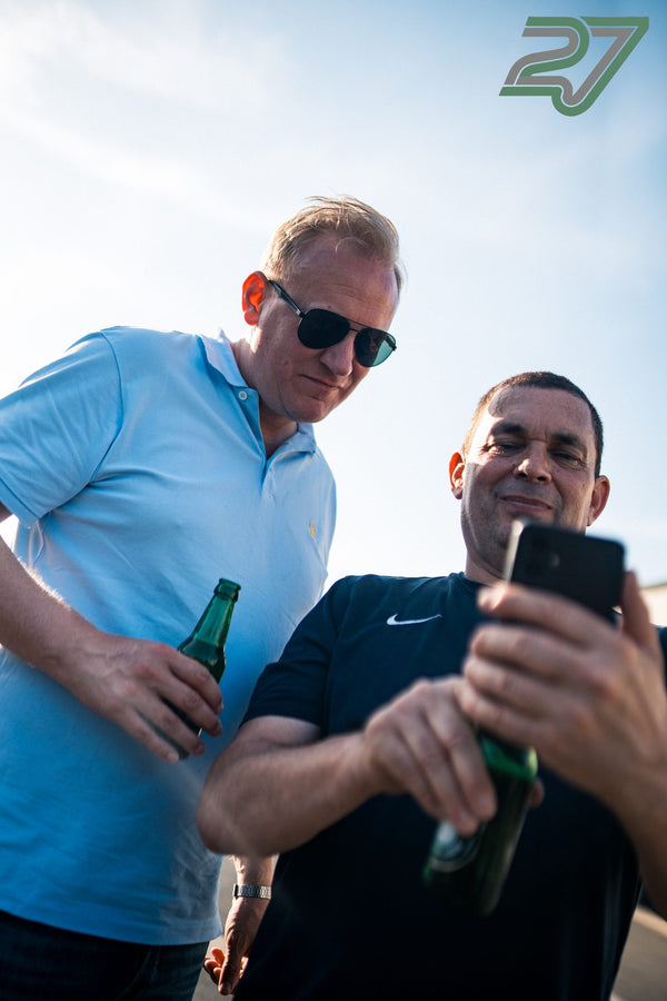 Zwei Männer schauen lachend auf ein Smartphone, beide halten eine Bierflasche in der Hand