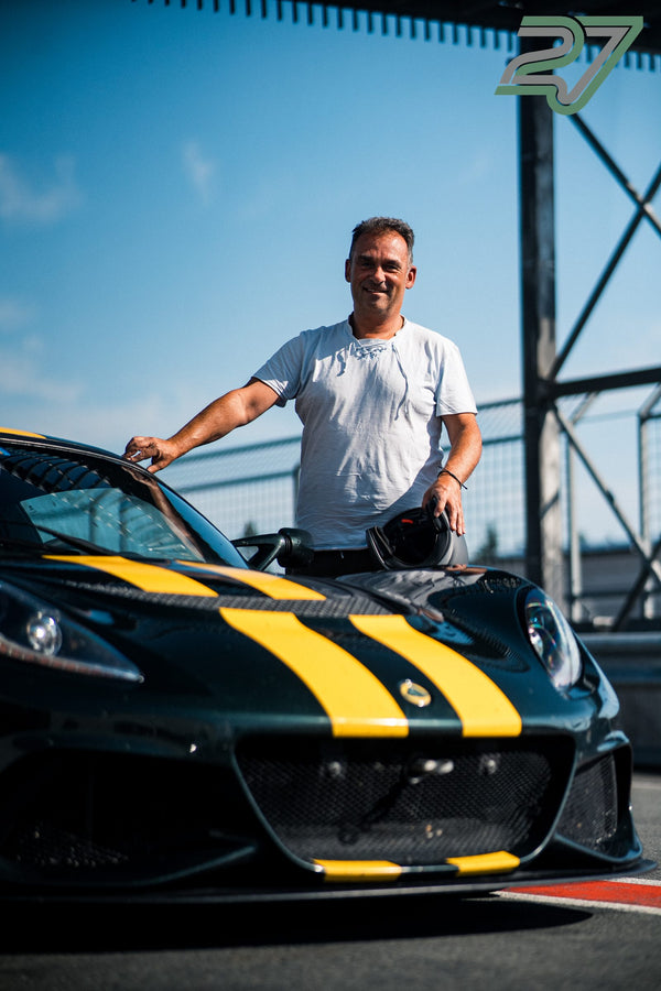 Ein Mann steht lächelnd neben seinem dunkelgrünen Lotus mit gelben Streifen, den Helm in der Hand