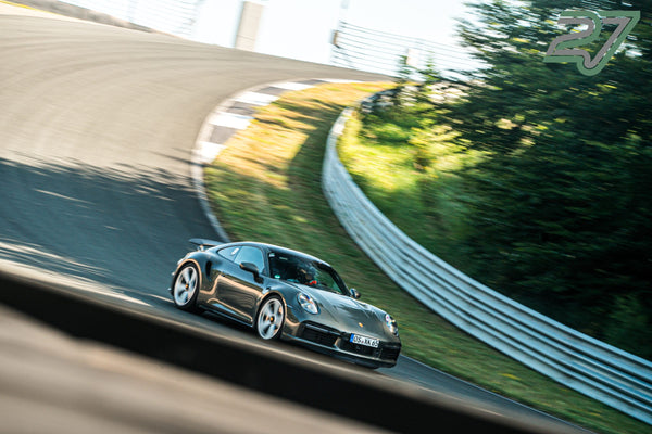 Grauer Porsche 911 neigt sich in eine Kurve, Mitzieher-Aufnahme mit verwischten Bäumen im Hintergrund