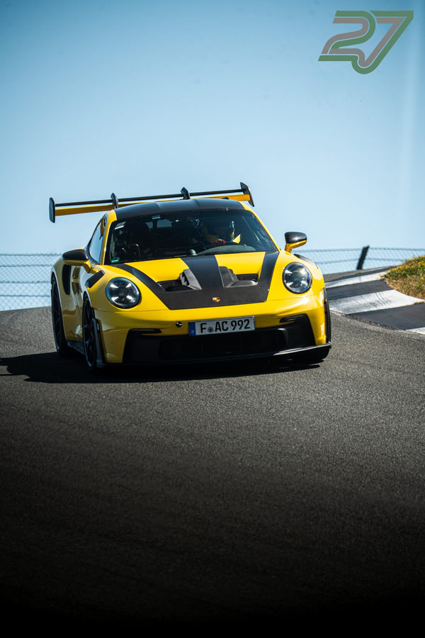 Ein gelb-schwarzer Porsche 911 GT3 RS kommt über eine Kuppe von Bilster Berg vor klarem Himmel