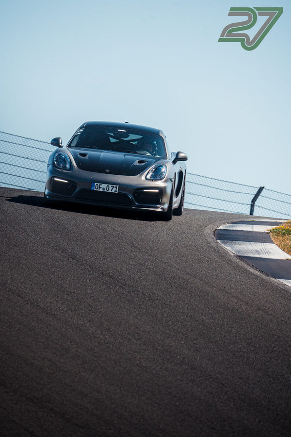 Mattgrauer Porsche Cayman kommt über die Kuppe, Frontansicht bei strahlendem Sonnenschein