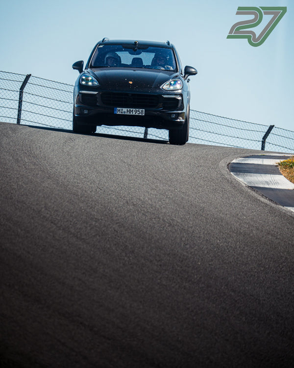 Schwarzer Porsche Cayenne fährt über eine Kuppe, Frontansicht vor klarem blauem Himmel