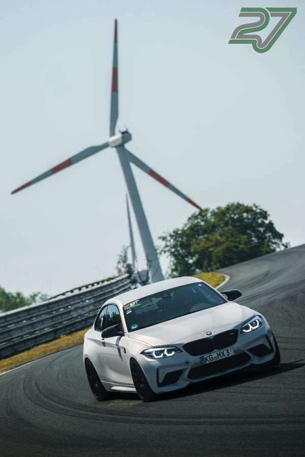 Ein weißer BMW M2 kurvt vor einem der Windräder am Horizont von Bilster Berg