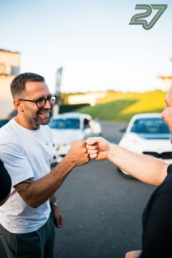 Zwei Männer geben sich lachend die Faust, im Hintergrund parken weiße Fahrzeuge auf dem Gelände