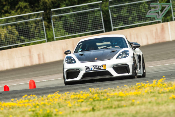 Ein weißer Porsche Cayman GT4 RS fährt am Bilster Berg durch eine Kurve mit orangen Pylonen und gelben Wiesenblumen