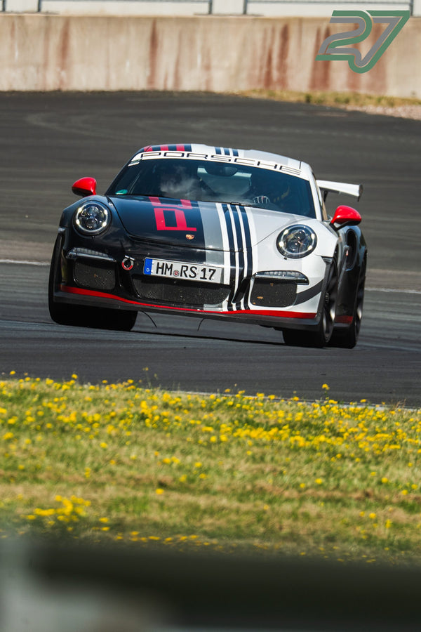 Ein schwarz-weißer Porsche 911 mit roten Streifen fährt an einer gelben Blumenwiese vorbei