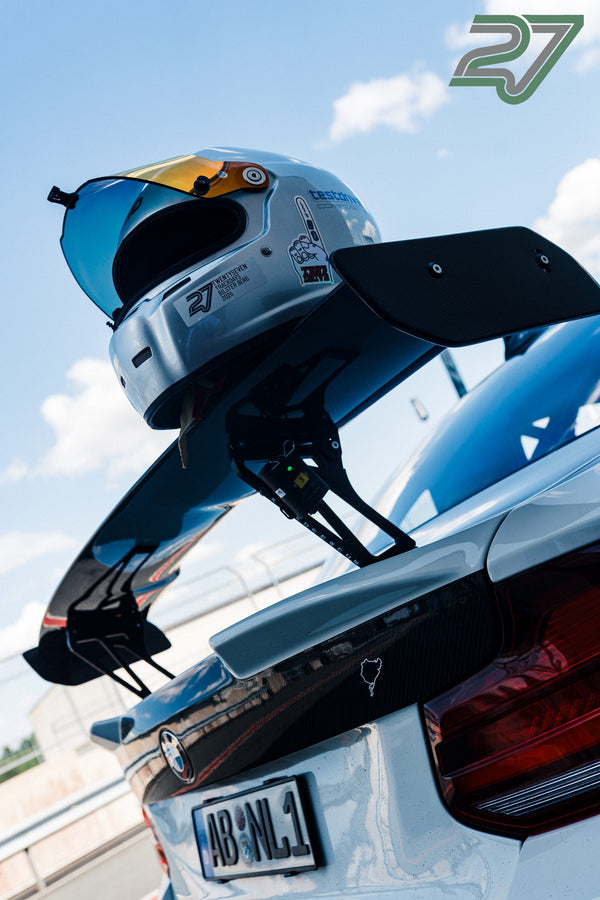 Weißer Helm mit verspiegeltem Visier lehnt am Heckflügel eines weißen BMW vor blauem Himmel