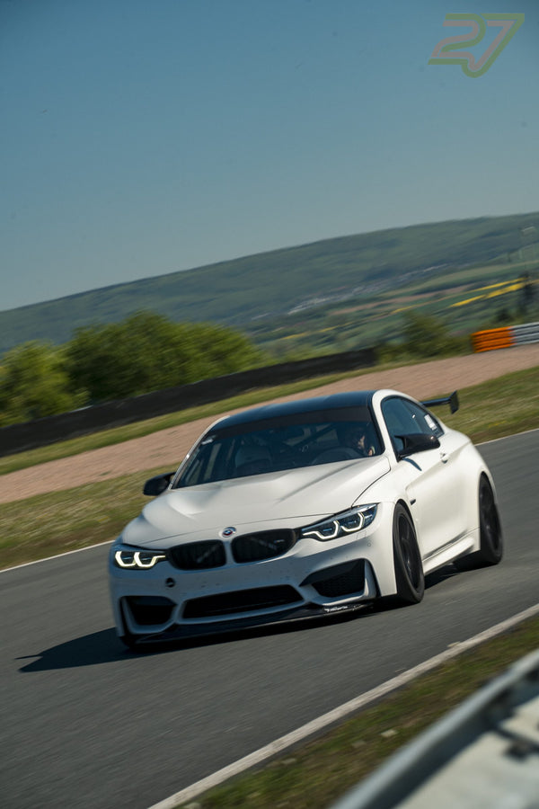 Weißer BMW mit schwarzem Dach und hohem Heckflügel rollt in Frontalansicht durch die Kurve