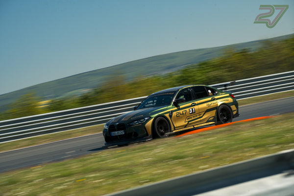 Grün-goldener BMW mit 247-Rennlackierung fährt in Schräglage durch eine schnelle Kurve