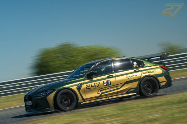 Grün-goldener BMW mit großem Heckflügel gleitet seitlich durch eine sonnige Streckenkurve