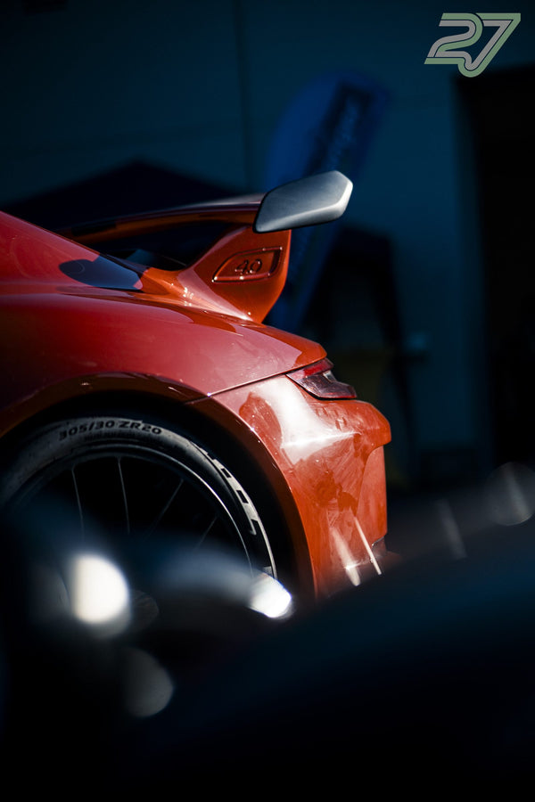 Nahaufnahme vom Radhaus und Heckflügel eines orangefarbenen Porsches im Abendlicht