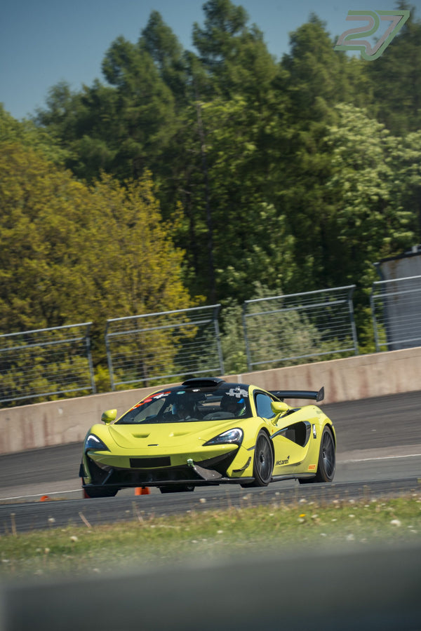 Gelbgrüner McLaren mit Startnummer 4 fährt frontal durch eine Kurve, Wald im Hintergrund
