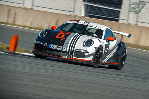 Weiß-schwarzer Porsche 911 Cup-Rennwagen mit Startnummer 17 neigt sich am Kurvenausgang, orange Pylonen säumen die Strecke