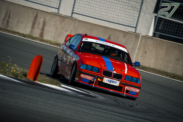 Roter BMW M3 mit blauem Streifen und Startnummer 14 kurvt an einem orangen Pylon vorbei, Fahrer mit Helm sichtbar