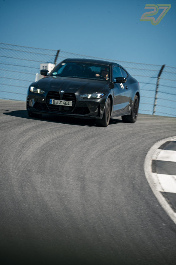 Schwarzer BMW M4 fährt frontal auf die Kamera zu, Streckenmarkierung 11 und blauer Himmel im Hintergrund