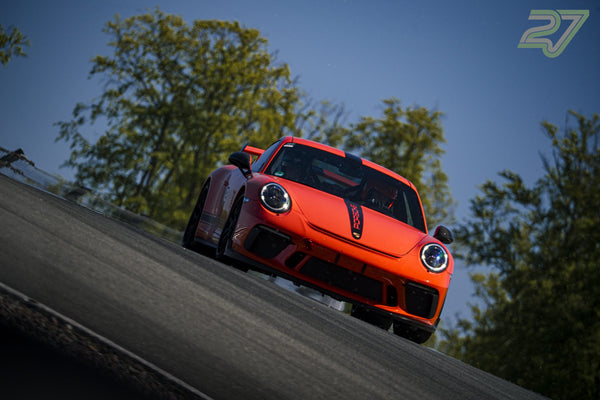 Roter Porsche 911 Rennwagen mit schwarzem Streifen fährt frontal bergab, Bäume säumen die Strecke