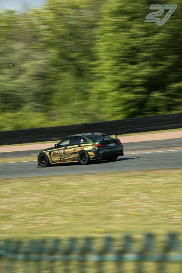 Dunkelgrüner BMW mit goldenen Akzenten zieht als Mitzieher-Aufnahme durch die Kurve, Bäume verschwimmen