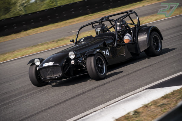 Schwarzer Caterham mit offenem Cockpit und Überrollkäfig, Fahrer mit Helm gut sichtbar