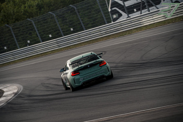 Mintgrüner BMW M2 mit TWENTYSEVEN-Beschriftung fährt leicht quer aus der Kurve, Reifenspuren auf dem Asphalt