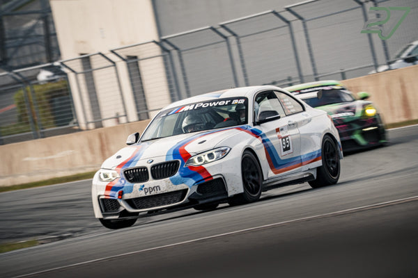 Weißer BMW-Rennwagen mit blau-roten M-Streifen führt knapp vor einem grünen Verfolger