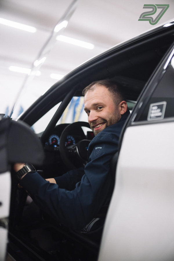 Ein lächelnder Teilnehmer sitzt mit offener Tür am Steuer eines Sportwagens beim Trackday