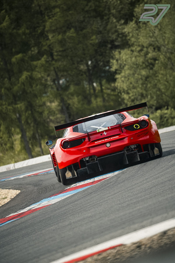 Roter Ferrari 488 GT3 fährt von hinten durch eine schattige, von Wald gesäumte Kurve