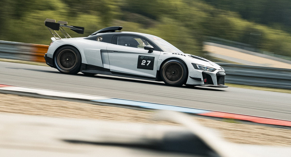 Weißer Audi R8 GT3 mit Startnummer 27 rast in Seitenansicht an grüner Hügelkulisse vorbei in Brünn