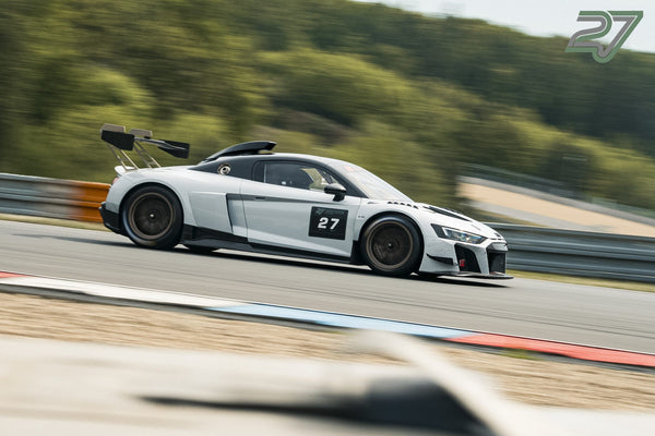 Weißer Audi R8 GT3 mit Startnummer 27 rast in Seitenansicht an grüner Hügelkulisse vorbei