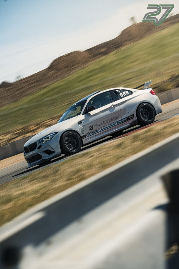 Weißer BMW M2 mit auffälligen Renn-Decals liegt in dynamischer Schräglage in der Kurve