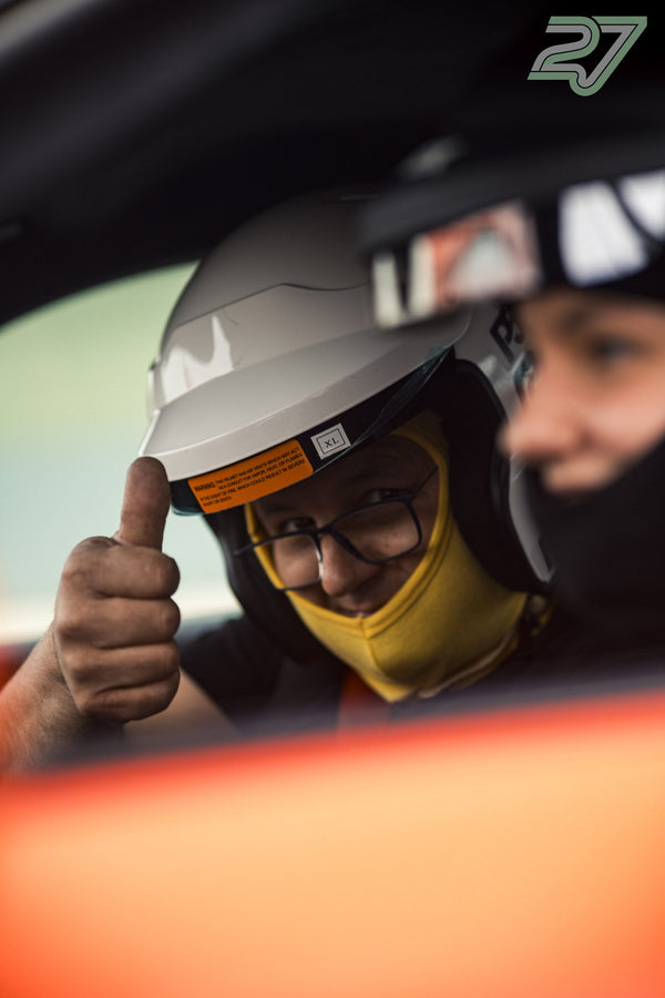 Ein Fahrer mit Brille und gelber Sturmhaube streckt lachend den Daumen aus dem Cockpit
